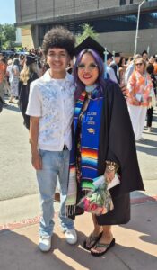 Michael Lama Jr. (left side) is wearing a white button up with a blue-floral patch stitching. He is wearing light denim jeans with white tennis shoes and has curly hair. Desiree Lama (right-side) wears a cap and gown with a blue sash while holding roses. She has purple hair. They are both smiling. 